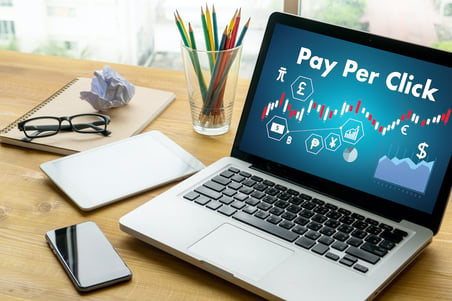 open laptop computer sitting on a financial advisors desk with pay per click written on the screen