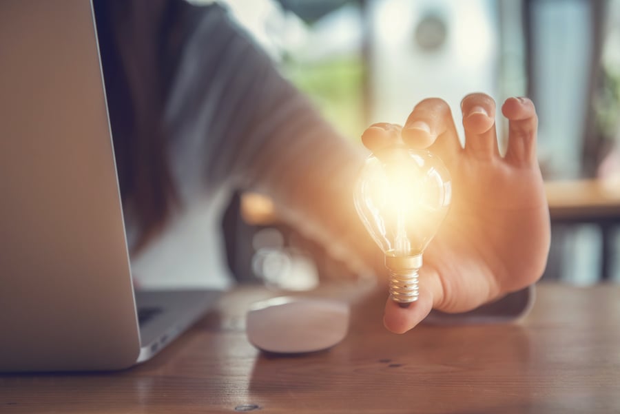 financial advisor holding an illuminated lightbulb in front of laptop signifying productivity