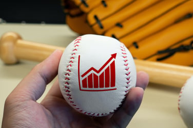 a financial advisor holding a baseball that has an upward arrow in red painted on the cover of the ball representing positive client growth